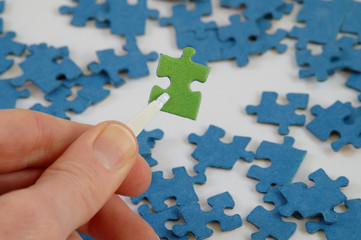 Hand holding one green jigsaw puzzle piece with Tweezers, blue and white background