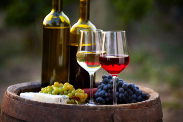Pair of wine glasses and bottles on old barrel with bunch of grapes