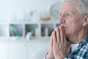 Sad senior man at home praying