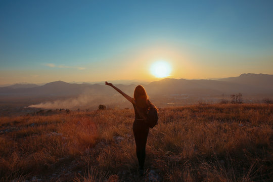Sunset mountain. Tourist Free happy  woman outstretched arms with backpack enjoying life in wheat field. Hiker cheering elated and blissful with arms raised.