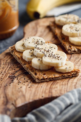 Fototapeta na wymiar Two multi grain breads with peanut paste, banana slices and chia seeds on a serving wooden board. The concept of healthy fitness breakfast.