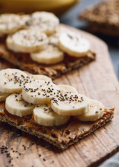 Two multi grain breads with peanut paste, banana slices and chia seeds on a serving wooden board. The concept of healthy fitness breakfast.