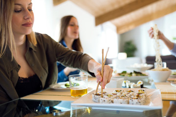 Two beautiful young women eating japanese food at home.