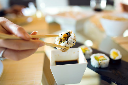 Woman's hand picking up sushi with chopsticks.