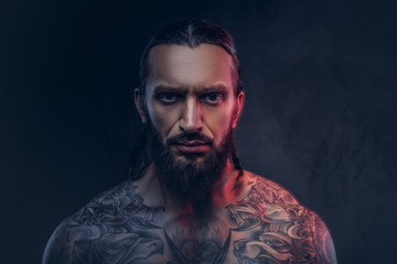 Close-up portrait of a muscular bearded tattoed male with a stylish haircut, isolated on a dark background.