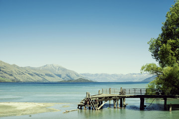 Muelle de madera derruido y viejo junto a un lago de agua azul frente a paisaje de montañas y cielo azul despejado