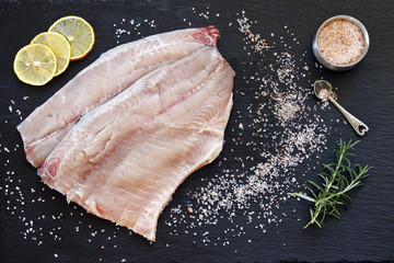 Close-up photo of fresh raw fish fillet with sea salt and lemon on black concreted table background