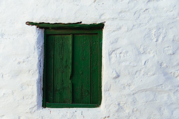 A small green wooden window in a white stone wall