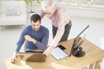 Senior businessman giving adice to her young colleague. Sales assistant sitting in front of laptop and consulting with senior manager while working together on new project. Teamwork at the office. 