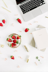 Home office desk with laptop, notebook, lipstick, fresh raw strawberries and rose flower buds on white background. Flat lay, top view.