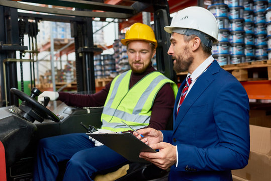 Waist up portrait of mature businessman talking to warehouse worker sitting in forklift car, copy space