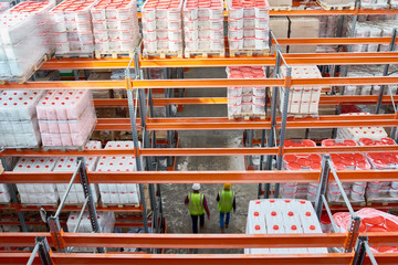 High angle background image of tall shelves in modern warehouse with two workers wearing hardhats walking in aisle, copy space
