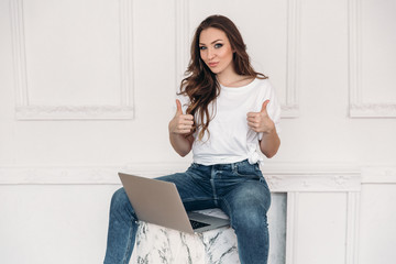 happy girl freelancer after a successful deal is happy and hands showing ok sign. Business lady works at the computer. A housewife woman with a laptop in a bright beautiful office. Human emotions.