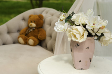 vase with beautiful flowers on the table near the sofa with bear toy
