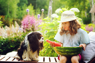 summer happy child girl eating watermelon outdoor on vacation, and sharing it with her dog