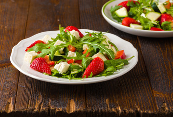 Fresh vegetable strawberry salad on white plate on natural rustic desk.