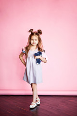 Pretty joyful girl in a pink dress, with long brunette hair, on a pink background. Beautiful sweet moments of a little princess, pretty friendly child, having fun looking at the camera