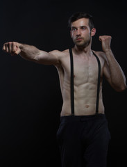 young man boxing with braces on pants on black background
