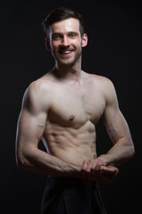 young man with muscles looking on camera smiling on black background