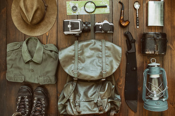 Camping stuff arranged on wooden backdrop. Machete, shirt, boots, lantern, smoking pipe, hat, map, compass.  Getting ready for a hike concept. Trekking postcard, poster, banner.