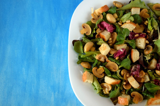 Salad with lettuce, champignons, pine nuts and croutons on a white plate on blue background