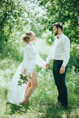 stylish bride in silk dress and groom in suit walking in sunny garden on wedding day. luxury wedding couple, happy newlyweds family. romantic moments.