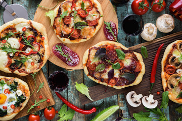 Pizza and wine party. Homemade rustic pizzas and raw ingredients served with red wine on oak chopping boards over shabby blue background