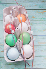White, gold, red, green and blue easter eggs with willow branches on  blue wooden background 