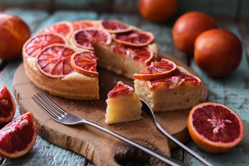 Delicious domestic pastry. Homemade fruit cake with blood orange slices on oak chopping board over rustic blue table