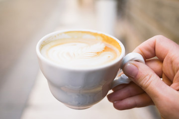 Woman's hand holding a white cup of coffee.