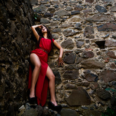 Sexy girl in red dress posing on old rock castle with long legs beauty makeup and passion glamour