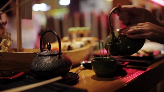 Girl pours tea in a Japanese restaurant on the big sushi set and family over dinner