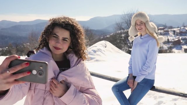 Girls friends making mobile photo at snowy mountain landscape