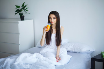 Cheerful woman drinking an orange juice sitting on her bed at home