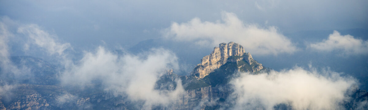 Mountaintops covered with clouds during sunrise panorama, a rocky top at Puertos de Beceite national Parc in between of clouds