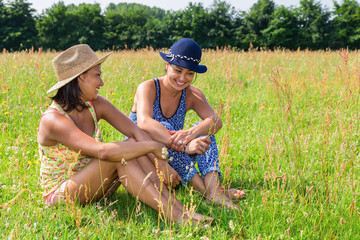 Two laughing women sit in blooming meadow