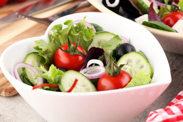 bowl of salad with vegetables and greens, with tomato, cucumber and onions.