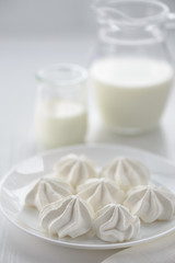 meringues in a plate and with a jug of milk on a white background