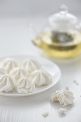 Fototapeta na wymiar meringues in a plate with green tea in a kettle on a white background