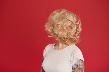Concept shot of blonde girl looks back and show her curly hair. Isolated over red background