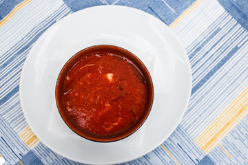 Vegetable soup gazpacho with mozzarella in a white plate on a blue tablecloth