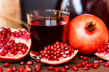 Ripe pomegranates with glass of juice on table