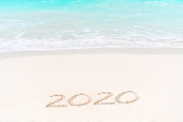 2020 handwritten on sandy beach with soft ocean wave on background