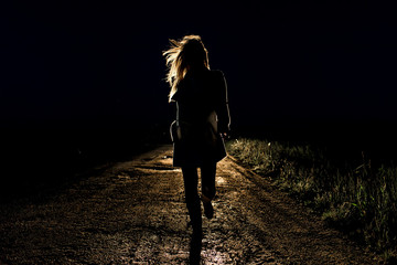 lonely young frightened woman on an empty night road runs away in the light of the headlights of...