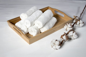Fototapeta na wymiar tray with a towel for hand in spa salon and a cotton branch on a white wooden table