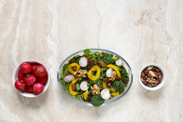 Healthy vegan salad with radish, nuts, yellow pepper on marble with copy space