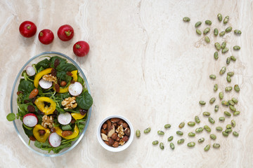 Healthy vegan salad with radish, nuts, yellow pepper on marble with copy space in middle