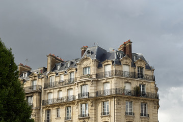 Fototapeta na wymiar Paris apartments before the storm. The last rays of sunlight strike the face of the building before clouds cut off the light. Paris, France.