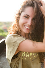 Outside portrait of glad beautiful woman with nude make up, long wavy hair and white teeth looking at camera and smiles, true emotions