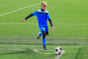 Teenage blonde Caucasian soccer (football) player in blue sport uniform is going to kick ball in...